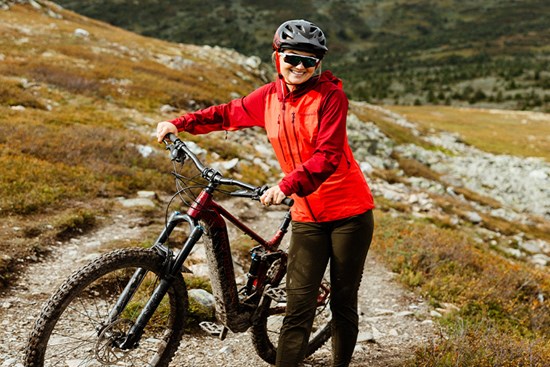 smilende dame med rød jakke, sykkelhjelm og sykkel