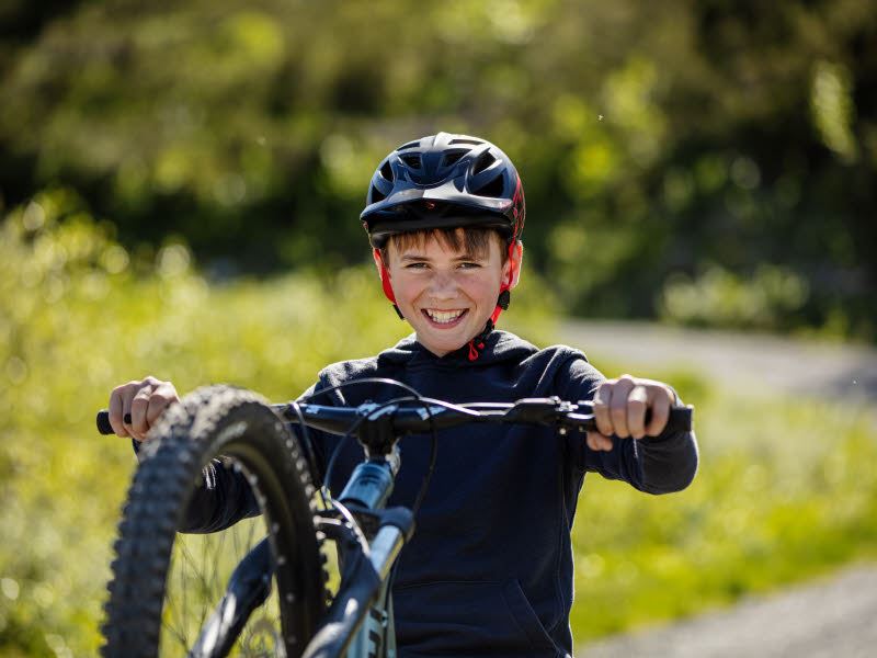 Smilende gutt med sykkehjelm som holder i rattet på sykkelen
