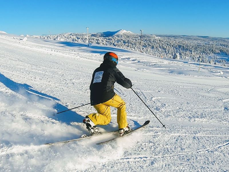 Bilde av en mann som står på telemarksski i alpinbakken på Skeikampen. Masse snø, blå himmel og strålende sol. 