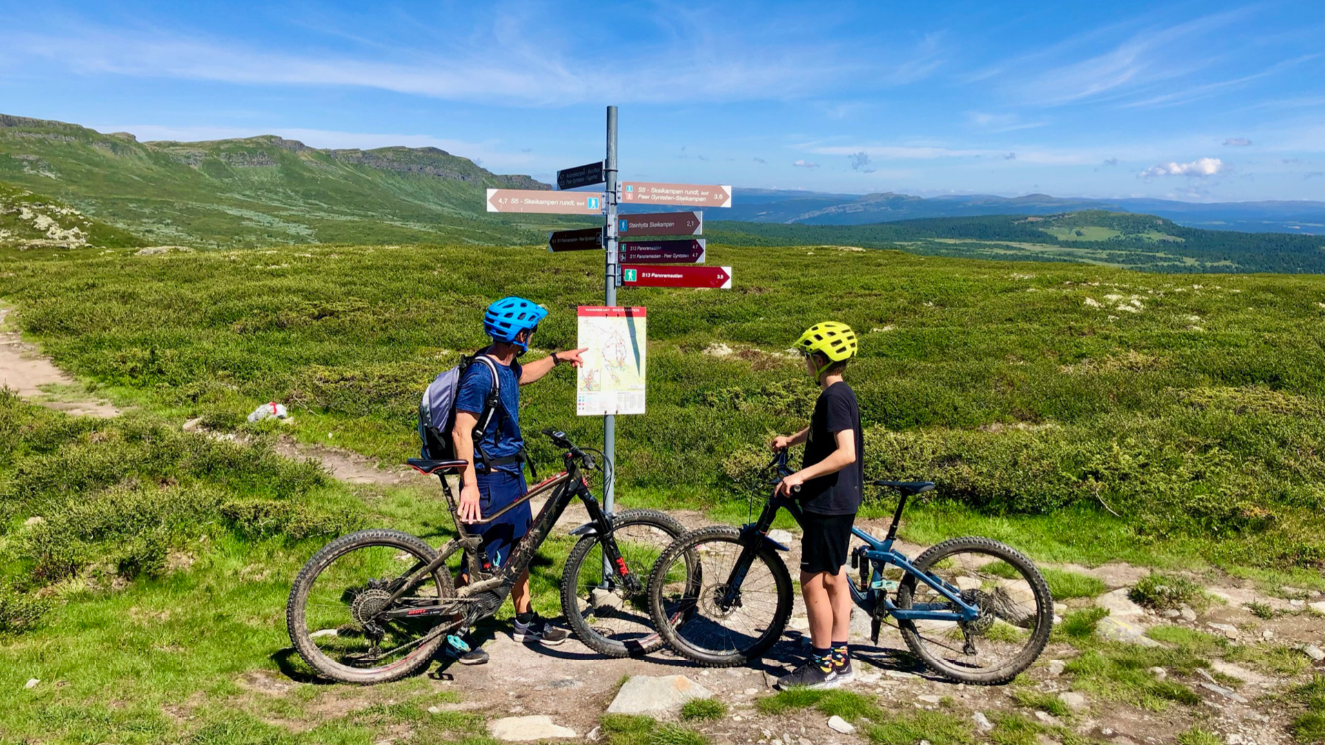 Mann og gutt på sykler på fjellet ved veiskilt