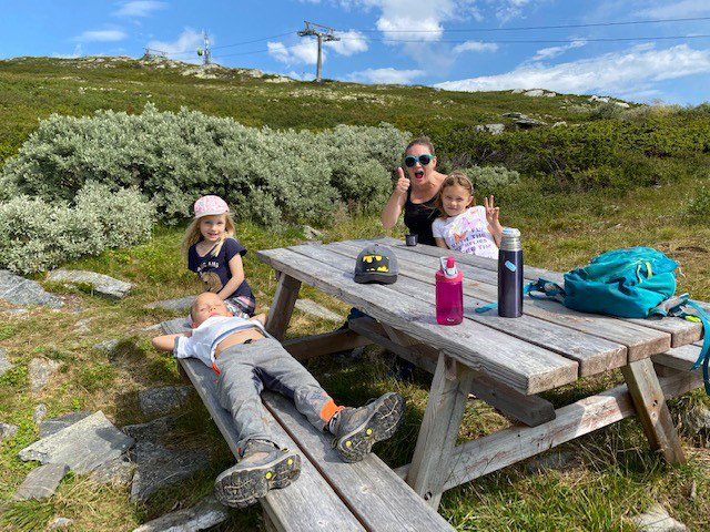 Familie på fire sitter på et bord med benker i naturen. Foto.